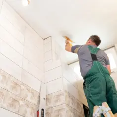 Fachowiec na drabinie nakłada gładź na sufit, obok piękne płytki na płytki.