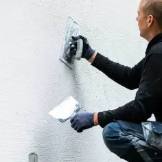 Murarz nakłada tynk na ścianę za pomocą kielni.