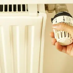 Dłoń reguluje termostat grzejnika, ustawiając temperaturę. To ważny element odpowietrzenia grzejnika, zapewniający komfort cieplny.