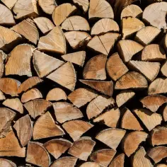 Stos drewna opałowego, idealnego na pytanie: jakie drewno do kominka? Widać słoje i pęknięcia, świadczące o jego naturalnym pochodzeniu.