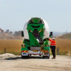 Robotnik przy betoniarce, zastanawia się ile kosztuje gruszka betonu. W tle koparka.