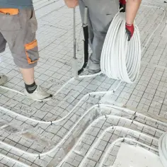 Pracownicy układają rury do ogrzewania podłogowego na siatce. Gotowa posadzka będzie ciepła i komfortowa.