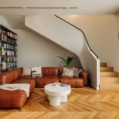 Nowoczesny salon z brązową kanapą, schodami i regałem z książkami.