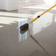 Wałek do betonu rozprowadza świeży anhydryt na podłodze z ogrzewaniem podłogowym.