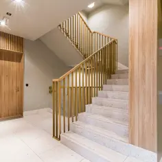 Nowoczesna klatka schodowa z drewnianą okładziną i złotymi balustradami. Praktyczne ściany na klatce schodowej dodają ciepła i elegancji.