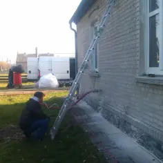 Prace przy domu, montaż elewacji wentylowanej. W tle białe busy i pracownicy.