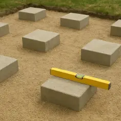 Układanie betonowych kostek pod przyszły taras. Poziomica na jednej z nich gwarantuje równość.
