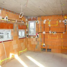 Rozprowadzona instalacja elektryczna w nowym budynku, z widocznymi przewodami i puszkami na ścianach z cegły.