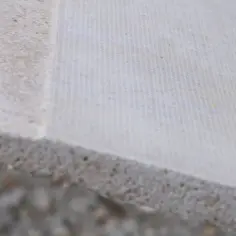 Brzeg płyty mgo z widoczną strukturą, pokryty jasnym materiałem o drobnej siateczce.