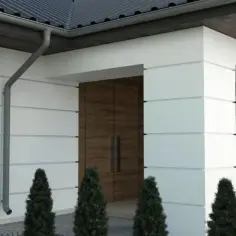 Nowoczesny dom z białym tynkiem i drewnianymi akcentami. Eleganckie boniowanie elewacji podkreśla geometryczne kształty budynku.