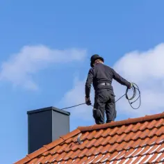 Kominiarz na dachu z narzędziami. Zastanawiasz się, ile kosztuje czyszczenie komina?