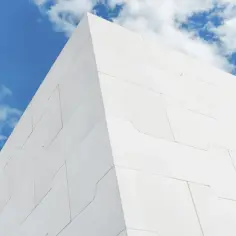 Nowoczesna biała fasada z geometrycznymi płytami, idealna dla systemu 3e cena m2. Błękitne niebo z chmurami w tle.