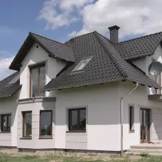 Nowoczesny dom z jasną elewacją i ciemnym dachem. Okna w brązowych ramach, balkon i komin.