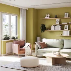 Jaki kolor do salonu? Jasnozielone ściany tworzą przytulną atmosferę, uzupełnioną przez pastelowy fotel i jasnoszarą kanapę.
