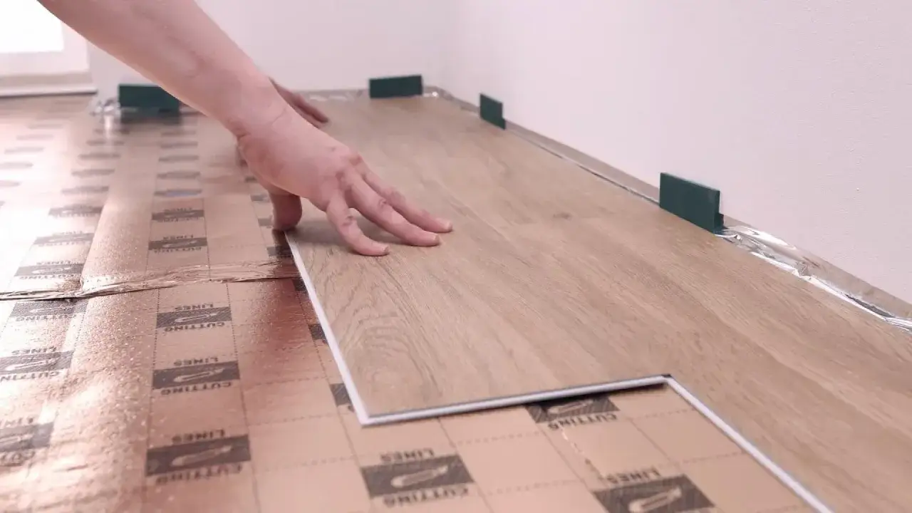 Układanie paneli laminowanych na podkładzie. Dłoń dociska panel do podłogi, która jest przygotowana do montażu.