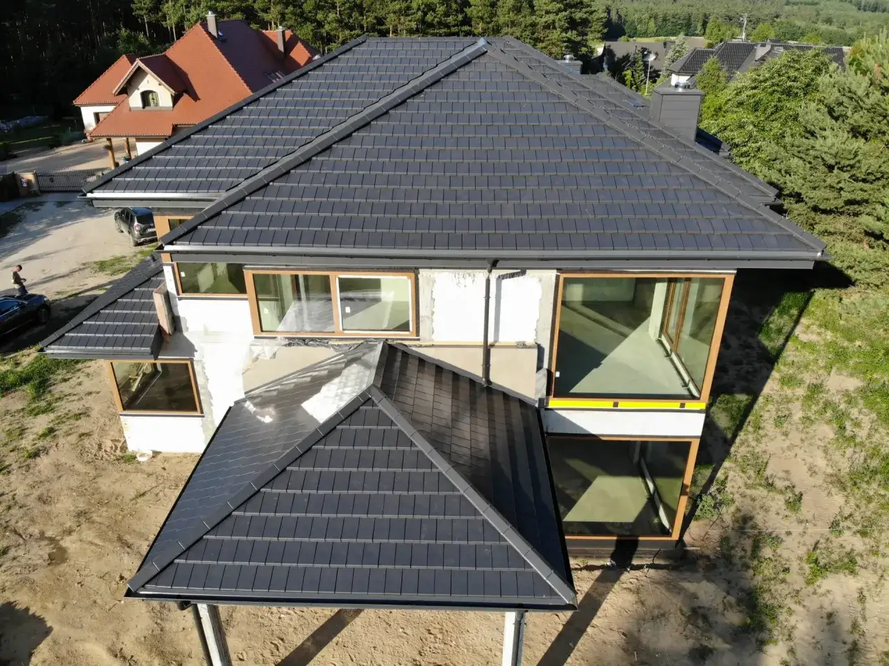 Nowy, ciemnoszary dach z dachówki ceramicznej na nowoczesnym domu. Trwa wymiana dachu, widać postęp prac.