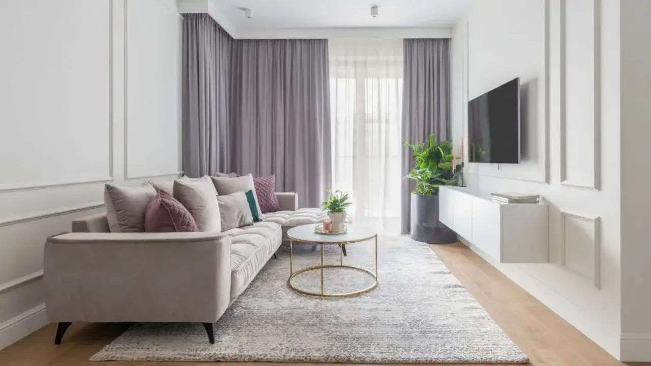 Elegancki salon z sofą w kolorze perłowym, szarymi zasłonami i nowoczesnym stolikiem kawowym.