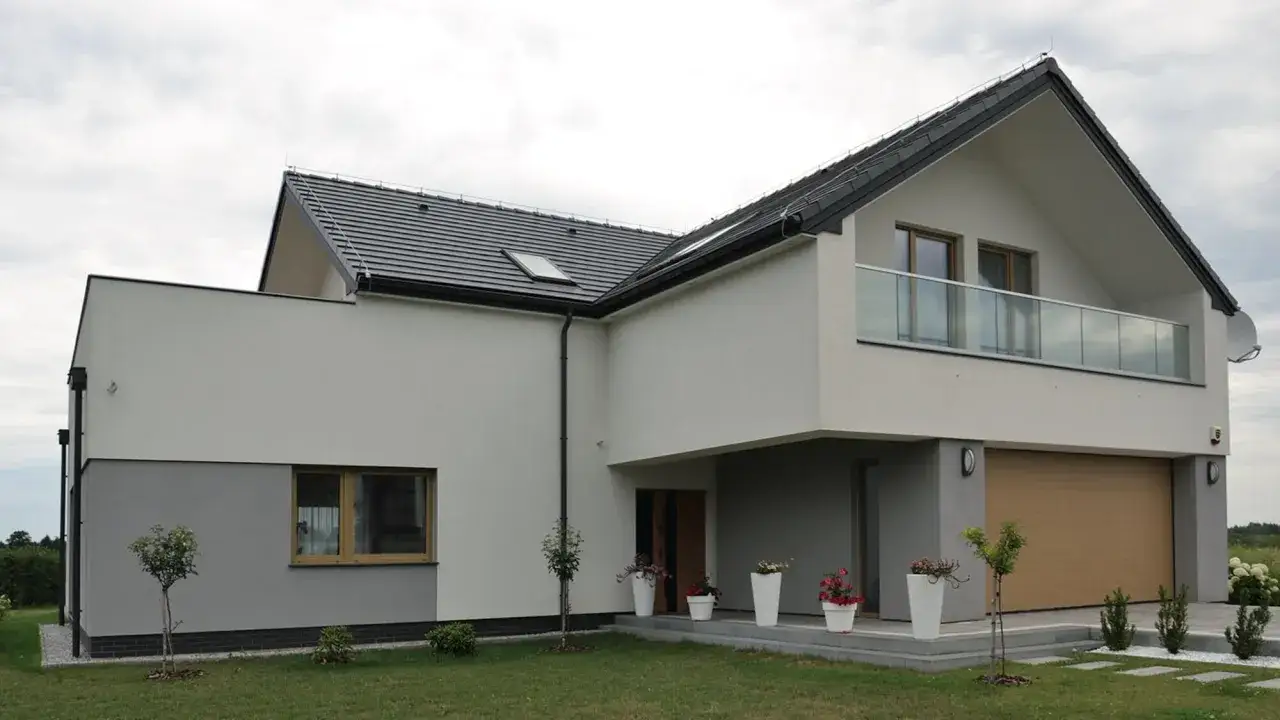 Nowoczesny projekt elewacji domu z szarymi i białymi tynkami, drewnianą bramą garażową i szklanym balkonem.