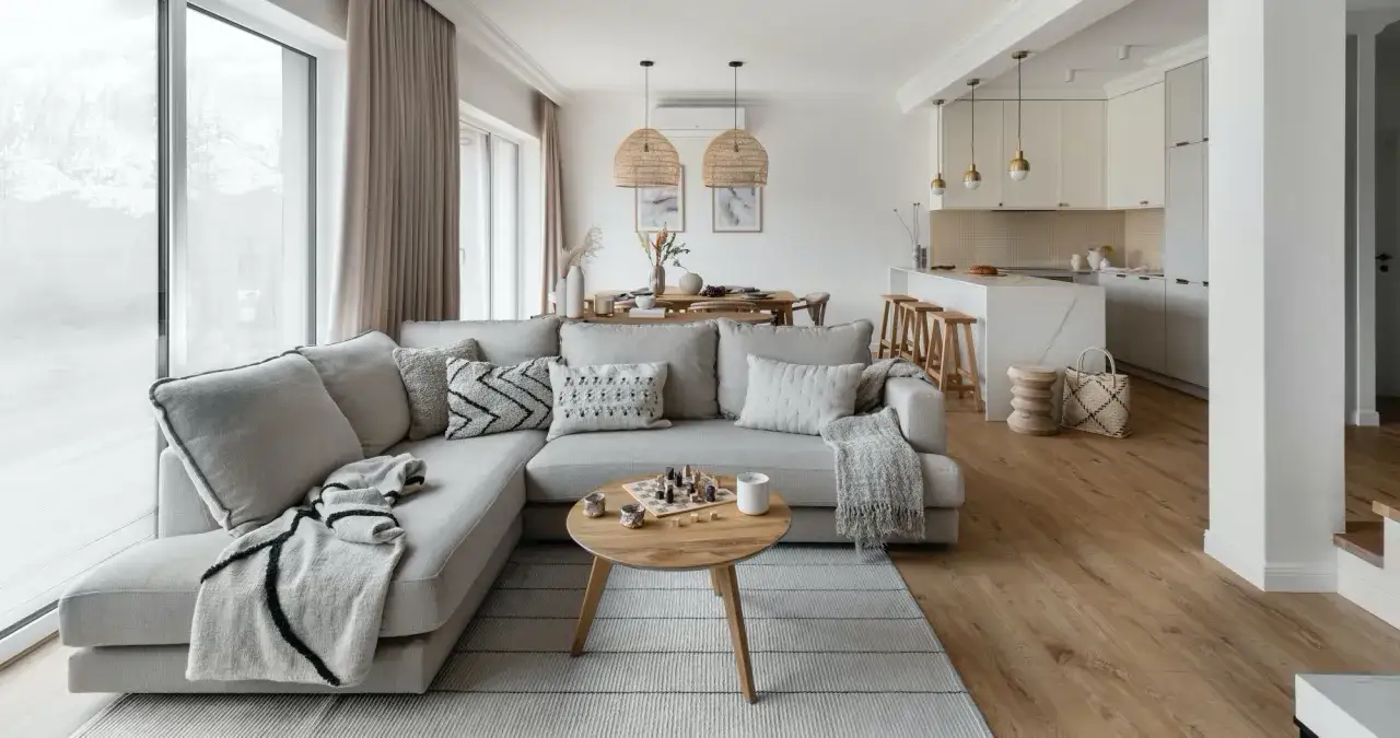 Przytulny salon z szarą sofą, drewnianym stolikiem i szachami. Ciepłe kolory drewna i tkanin tworzą relaksującą atmosferę.