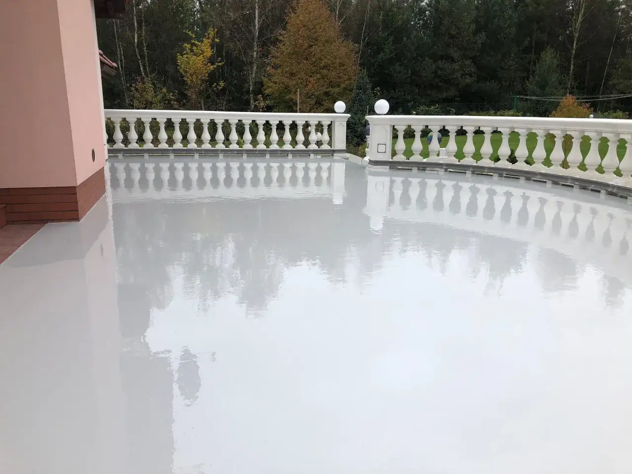Nowoczesna żywica na balkon cena za metr. Jasna, lśniąca powierzchnia odbija balustradę i drzewa.