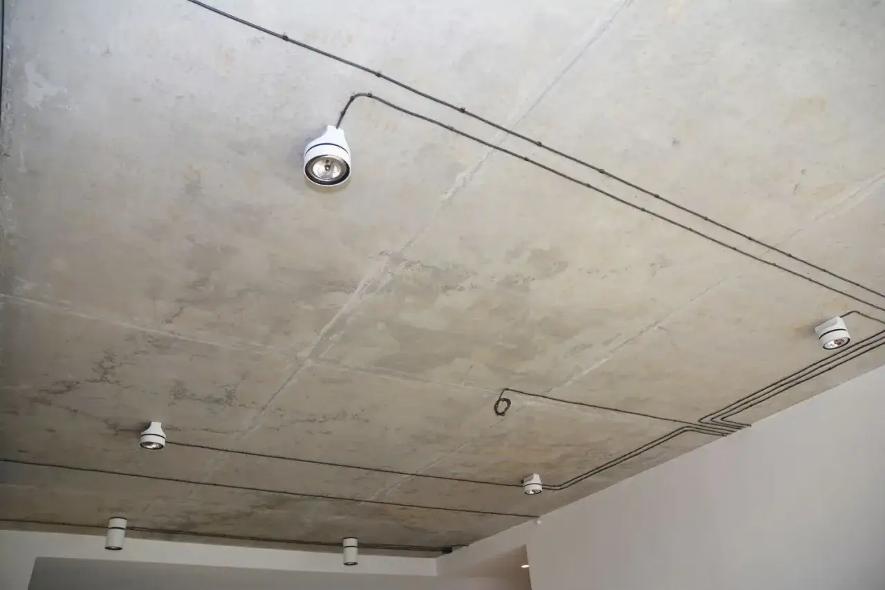 Nowoczesna instalacja natynkowa na betonowym suficie z kilkoma białymi reflektorami.