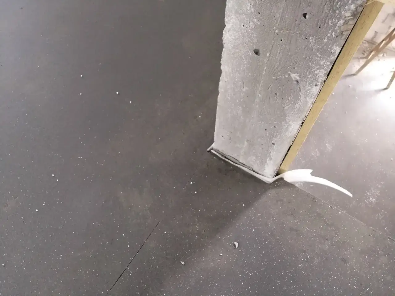 Szara posadzka z widoczną dylatacją przy betonowym słupie. Uszczelnienie wykonane pianką.