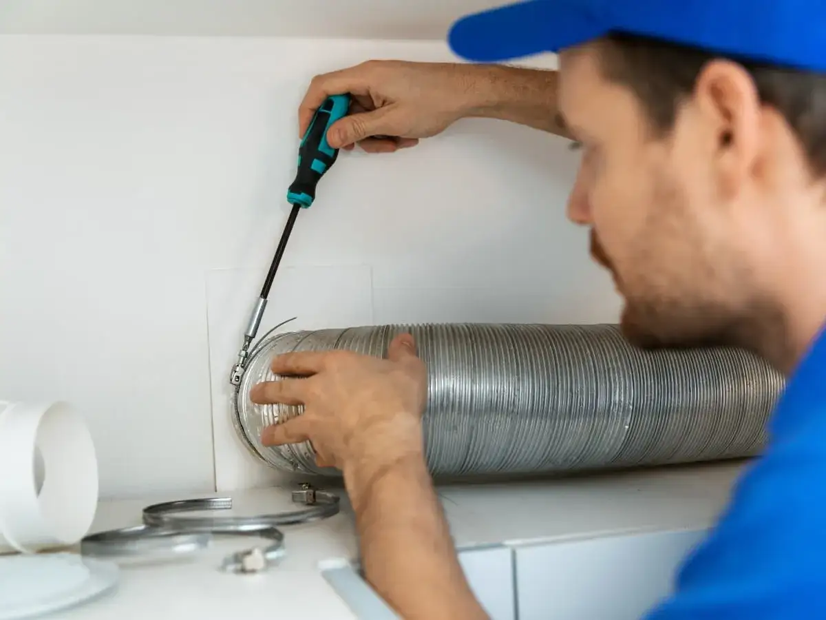 Instalator dokręca śrubę na metalowej rurze do okapu, używając wkrętaka.